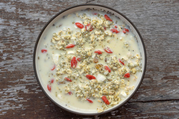 Fresh breakfast of granola, milk, nuts, goji berries, chia seeds and raisins. Muesli with fruits and berries in bowl on a wooden background