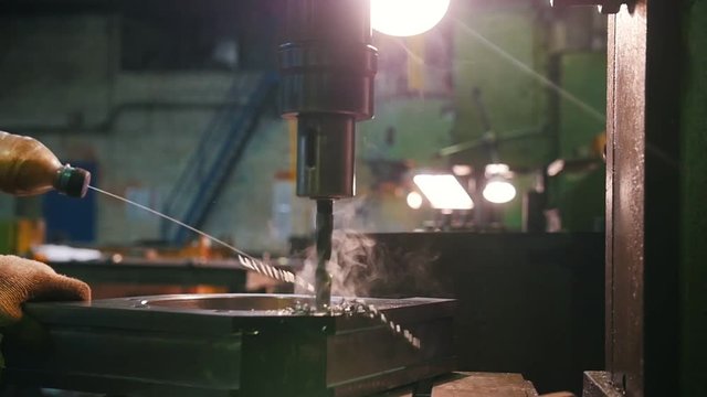 A man works with a drill for metal. It adds fluid to the material.