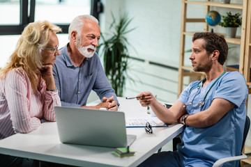 Male doctor pointing at laptop while talking with a senior couple.