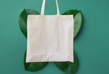 Blank white mockup linen cotton tote bag on green leaves foliage background. Zero waste reusable...