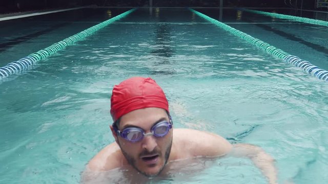 Young athletic man (25-30) crawl swimming at pool rests taking deep breaths after streneous exercise