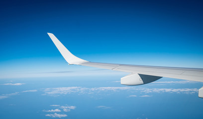 Fototapeta na wymiar Wing of plane over white clouds. Airplane flying on blue sky. Scenic view from airplane window. Commercial airline flight. Plane wing above clouds. Flight mechanics concept. International flight.