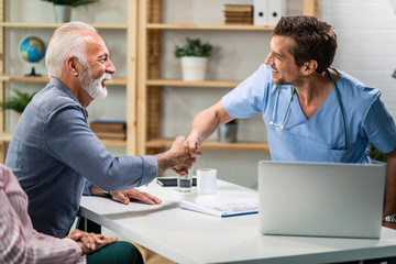 Happy senior man and doctor shaking hands while meeting at doctor's office.