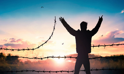 World Refugee Day concept: Man standing on barbed wire at sunset background