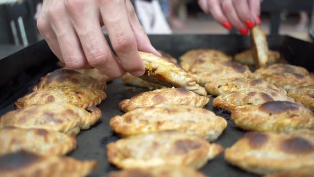 Removing hot empadadas from a baking dish with hands.