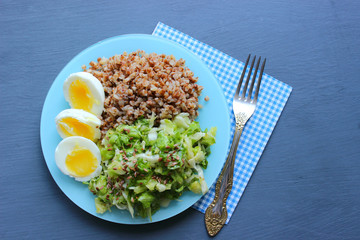 Buckwheat with vegetables. On a wooden background. The view from the top. Copy space. Healthy Breakfast with egg, salad and buckwheat porridge on a dark background. Proper diet. Diet menu.