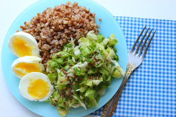 Buckwheat with vegetables. On a wooden background. The view from the top. Copy space. Healthy Breakfast with egg, salad and buckwheat porridge on a light background. Proper diet. Diet menu. 
