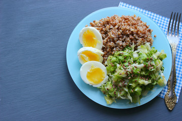 Buckwheat with vegetables. On a wooden background. The view from the top. Copy space. Healthy Breakfast with egg, salad and buckwheat porridge on a dark background. Proper diet. Diet menu.