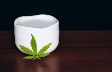 Macro close up of jar of cream from biological and ecological plants of hemp vegetable pharmaceutical oil CBD with green cannabis leaf with copy space