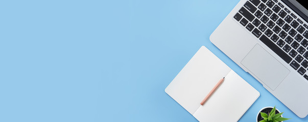 Girl write on open white book or accounting on a minimal clean light blue desk with laptop and accessories, copy space, flat lay, top view, mock up