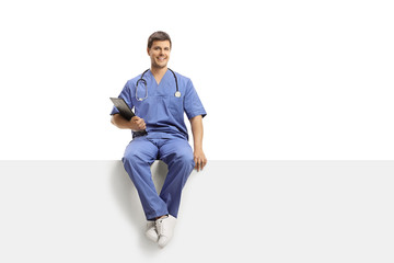 Young male doctor in a blue uniform sitting on a white panel