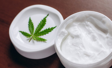 Macro close up of jar of cream from biological and ecological plants of hemp vegetable pharmaceutical oil CBD with green cannabis leaf with copy space