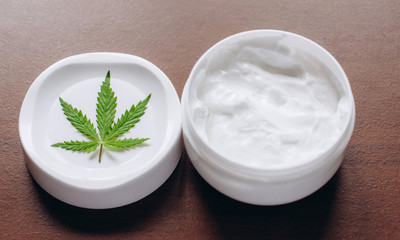 Macro close up of jar of cream from biological and ecological plants of hemp vegetable pharmaceutical oil CBD with green cannabis leaf with copy space