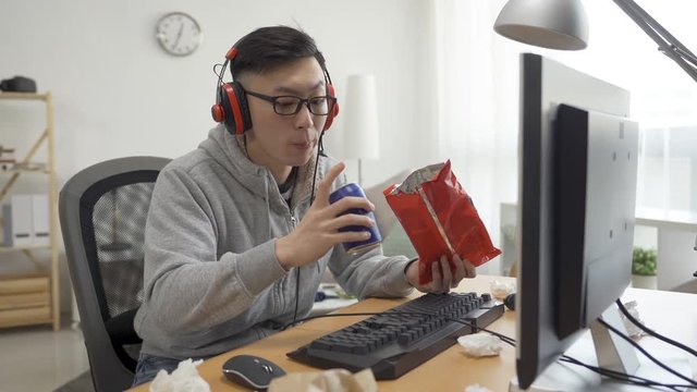 asian male homebody high school student love stay at home watching movie with junk food eating chip snack drinking beverage can on summer break holidays. nerd in glasses stare at computer with anime.