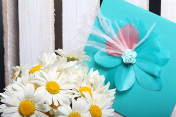 A bouquet of field daisies and a greeting card. On the background of wooden boards. Genus of perennial flowering plants of the Matricária family (Matricária).