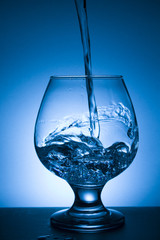glass of water with splash on blue background