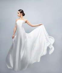Fototapeta na wymiar Fashion portrait of a beautiful woman in a waving white dress. Light fabric flies in the wind.