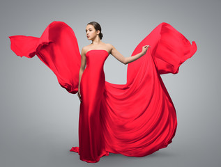 Fashion portrait of beautiful woman in waving red dress. Light fabric flies in the wind.