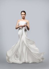Fototapeta na wymiar beautiful woman in a light fluttering white dress. Light fabric flies in the wind. Light gray background.