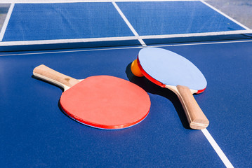 View of the table for playing table tennis. Two rackets and an orange ball. Sports equipment on the street. The concept of sports. Entertainment and active recreation
