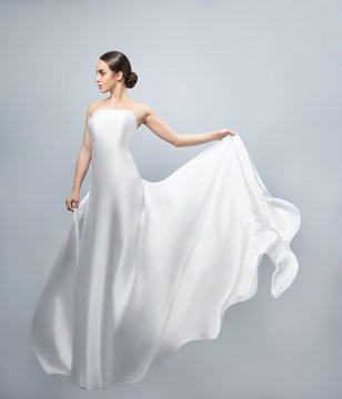 Fashion portrait of a beautiful woman in a waving white dress. Light fabric flies in the wind.