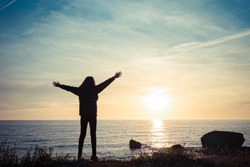 girl silhouette on sunset sea background. the girl rejoices with her arms wide apart.