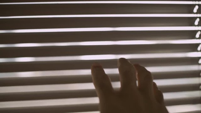 Camera follows a hand reaching over to open window blinds to peek outside