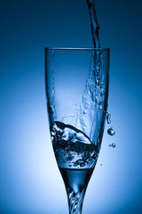 glass of water with splash on blue background