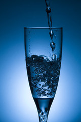 glass of water with splash on blue background
