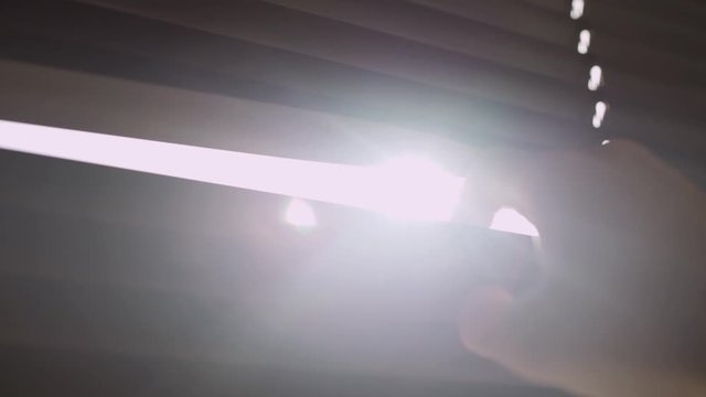 Close up - hand peeks through window blinds - sun shines through