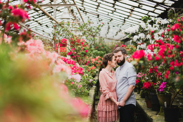 Young loving cheerful caucasian couple in glass greenhouse among colorful azalea flowers. Happy man...