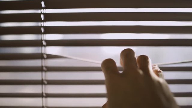 Close up of a hand reaching and opening a crack in the window blinds