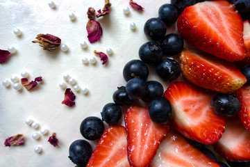 Close-up photo of a birthday cake decorated with white cream cheese frosting, fresh blueberries and slices of strawberries