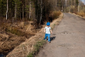 Early spring, a little boy of three years old in blue pants, one on a country road
