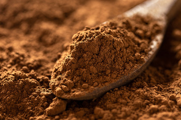 Detail of cocoa powder on a wooden spoon sitting on cocoa powder. Blurred background.