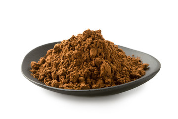 Cocoa powder in a black ceramic dish isolated on white.