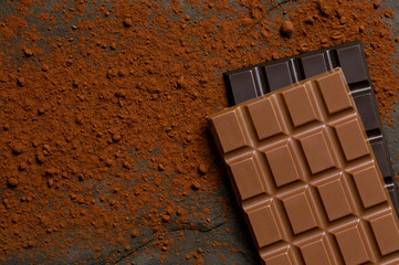 A slab of milk chocolate on top of a slab of dark chocolate on black slate dusted with cocoa powder from above. Space for text.