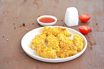Crispy chicken strips in cornflakes and parmesan cheese on a white plate. Selective focus. American cuisine.