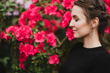 Naklejka premium Young beautiful caucasian woman in glass greenhouse among colorful azalea flowers. Art portrait of a girl wearing classic fashionable clothes.