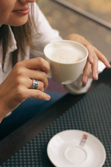 Woman with beautiful hands is drinking coffee in cafe. Close-up cappuccino in white cup, image with film effect and author processing.