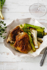 Roasted skin-on chicken thighs with leek and wine sauce on white distressed wooden table