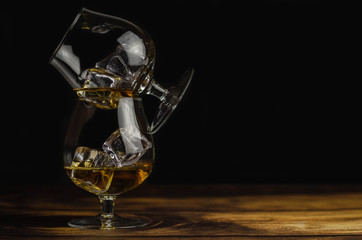 Two whiskey / cognac glasses with ice on a wooden background. Dark backdrop.