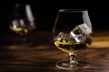 Two whiskey / cognac glasses with ice on a wooden background. Dark backdrop.