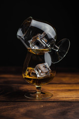 Two whiskey / cognac glasses with ice on a wooden background. Dark backdrop.