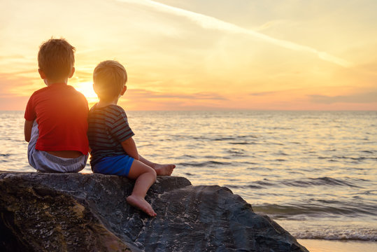 Two boys sitting on the rock at the beach at sunset