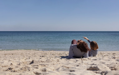 Walk moms with children on the beach. Sisters (8 and 7 years old) and younger brother (3 years old) are playing at sea.