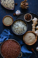 Various types of rice and grains with spices on blue background. Brown rice and mixed wild rice.