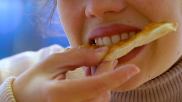 A young caucasian woman bites a piece of pizza and chews it. Slow motion