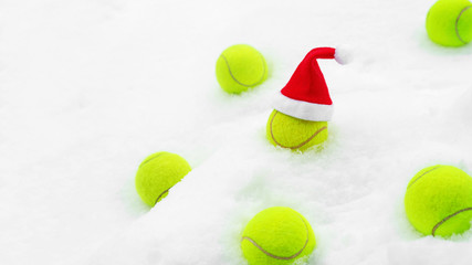 Tennis winter concept with tennis balls on white snow. Top view, copy space. Christmas New Year sport healthy layout. Santa Claus hat on the top off ball.