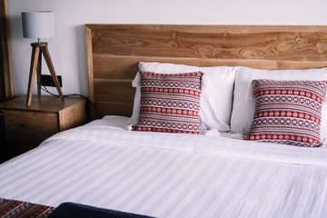 Bedroom interior, light wooden bedhead, wall, white bed sheets, red pillows. Minimal design